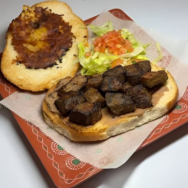 Open-faced sandwich with dark meat cubes, refried beans, lettuce, and diced tomatoes on a red plate.