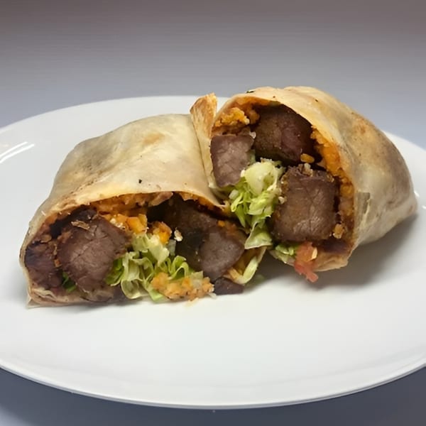 A large burrito, cut in half, revealing steak, rice, and lettuce on a white plate.