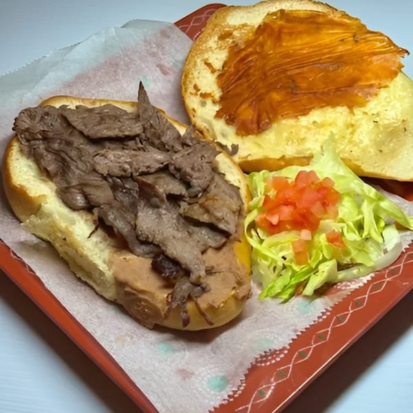 An open-faced steak sandwich with lettuce and tomato on a red tray with patterned paper.