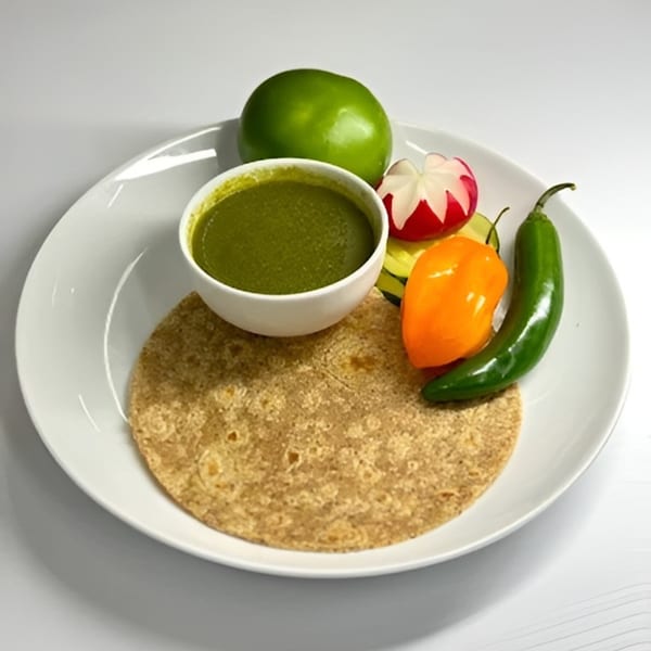 A tortilla, green sauce, lime, radish, and peppers on a white plate.