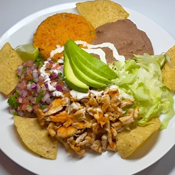 A colorful Mexican dish with chicken, rice, beans, avocado, salsa, lettuce, and tortilla chips.