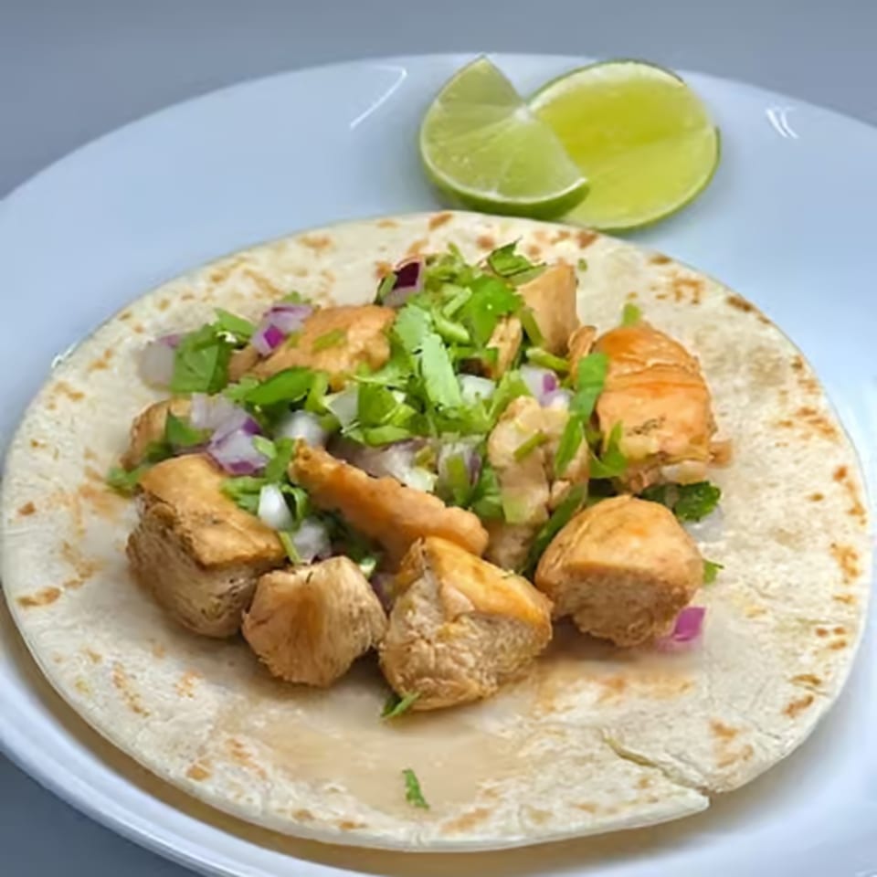 Chicken taco with cilantro, red onion, and lime wedges on a white plate.