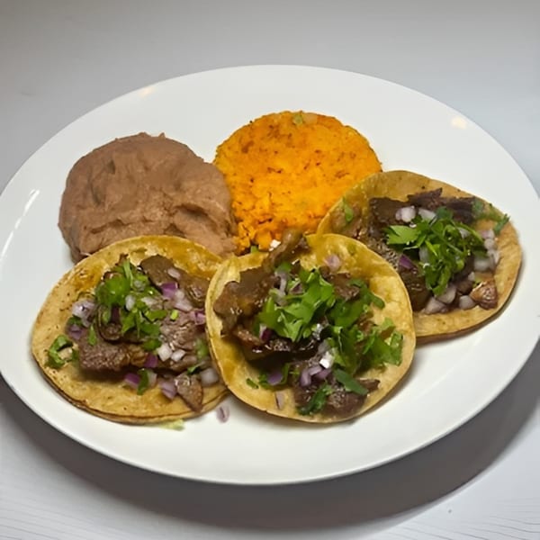 Three carne asada street tacos with cilantro and onions, served with refried beans and orange rice.