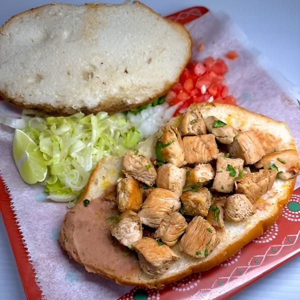 Open-faced chicken torta with refried beans, lettuce, onion, tomato, and a lime wedge.